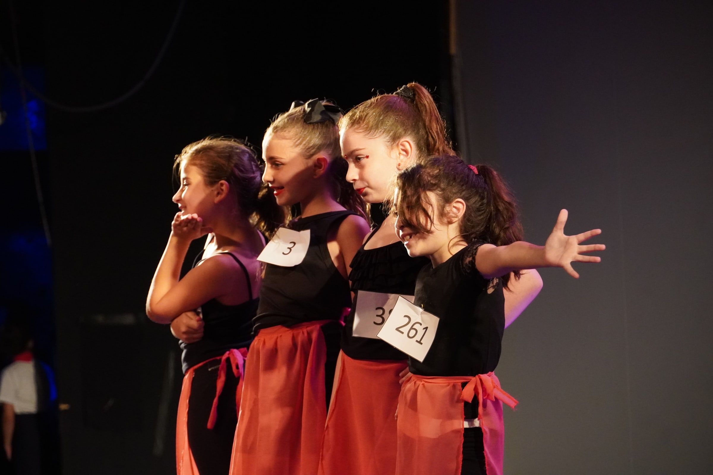 Alumnas con vestuario negro y rojo, de perfil, actuando una escena en el teatro.