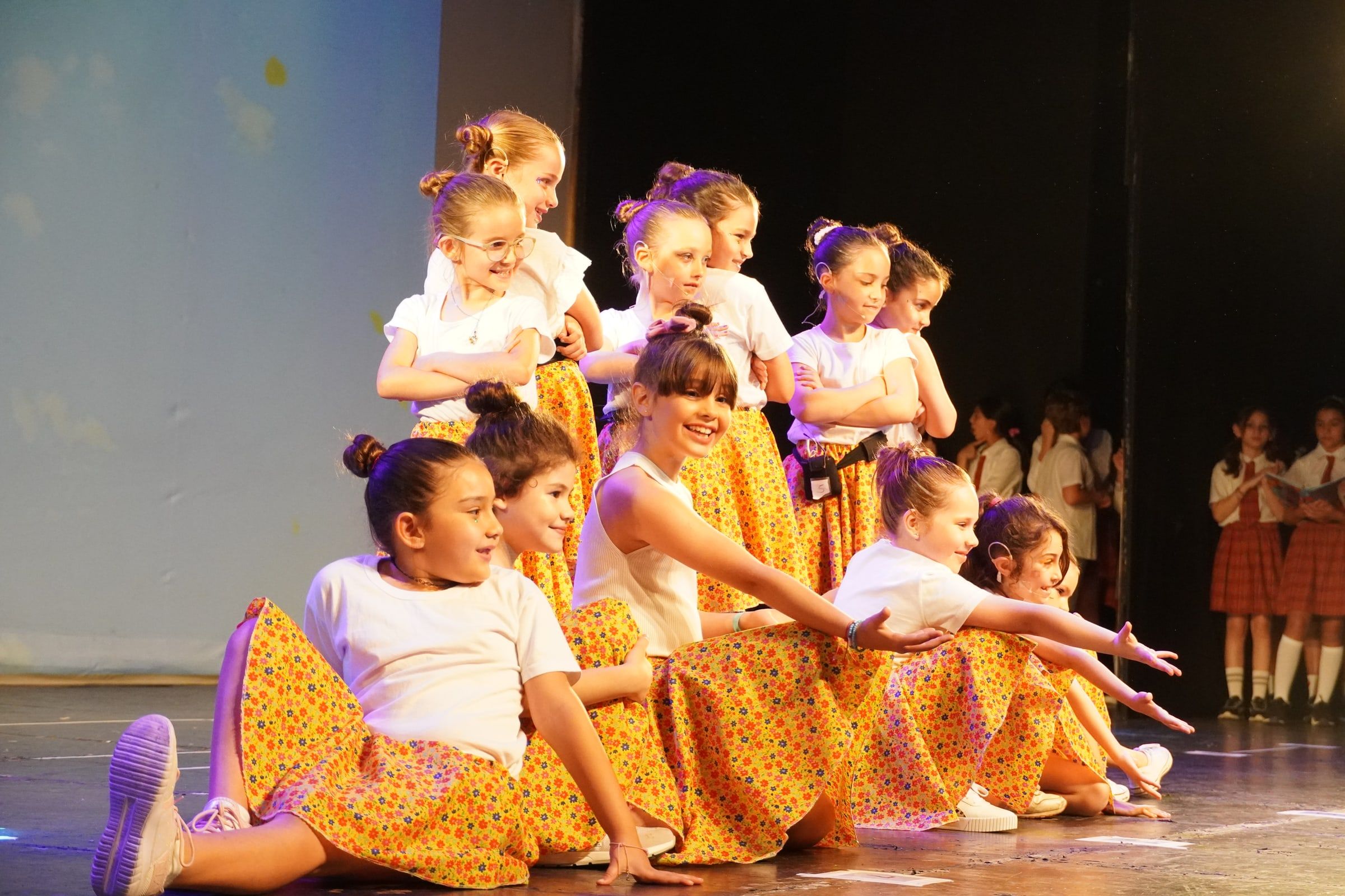 Las Mini Peques de La Trama, con polleras amarillas, en pose final sobre el escenario de un teatro.