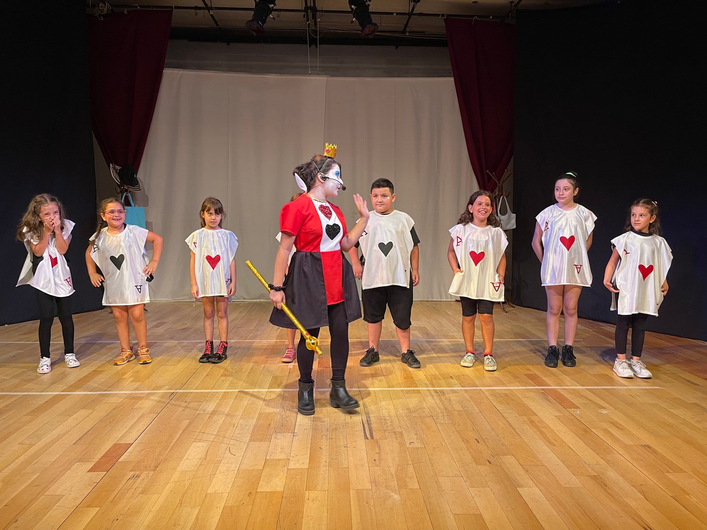 La Reina de Corazones y un grupo de chicos vestidos de cartas en la sala del estudio.
